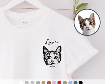 Puede incluir: Una camiseta blanca de manga corta con una ilustración en tinta negra de la cara de un gato en el pecho. Sobre la ilustración del gato, el nombre Luna está impreso en cursiva negra. Un recuadro circular muestra la fotografía original del gato.