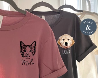 Puede incluir: Dos camisetas con retratos de mascotas personalizados. La camiseta de la izquierda es de color malva jaspeado con un retrato de gato en blanco y negro y el nombre "Milo". La camiseta de la derecha es de color asfalto con un retrato de golden retriever y el nombre "Luna".