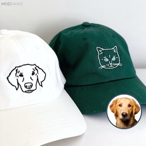 Puede incluir: Una gorra de béisbol blanca con el contorno bordado de una cara de perro en negro y una gorra verde oscuro con el contorno bordado de una cara de gato en blanco. El texto MODPAWS aparece arriba a la izquierda junto a una foto circular de un perro.