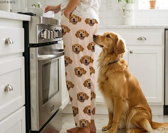 May include: Tan pajama pants with repeating golden retriever faces. A golden retriever dog sits attentively, looking up. The image is set in a kitchen with white cabinets and a stainless steel oven.