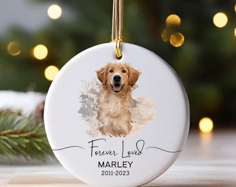 Könnte beinhalten: Ein rundes, weißes Keramikornament mit einem Golden Retriever-Porträt vor einem weichen Aquarellhintergrund. Der Text lautet Forever Loved, MARLEY und 2011-2023. Ein goldenes Band ist oben zur Aufhängung an einem Baum oder Ständer befestigt.