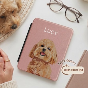 Puede incluir: Una funda rectangular para tableta en color rosa empolvado que presenta una ilustración personalizada de un perro de pelo rizado color marrón claro y el nombre LUCY impreso en letras mayúsculas blancas en la parte superior central.