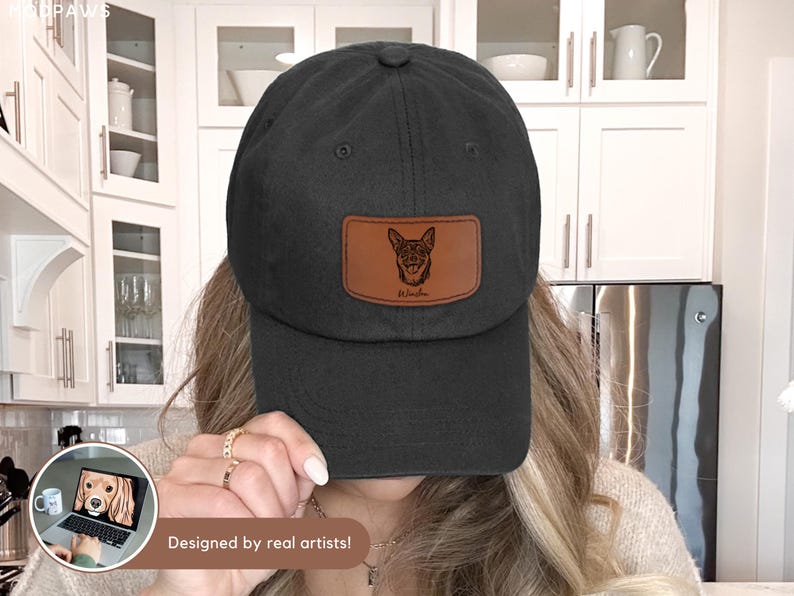 May include: Black baseball cap with a brown leather patch featuring a dog illustration and the name "Winston". The cap has a curved brim and a classic, casual style. The text "Designed by real artists!" is at the bottom.