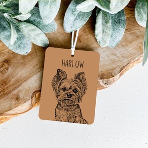 May include: A brown leather tag with a black and white illustration of a Yorkshire Terrier dog. The tag has the name "HARLOW" printed in black text.