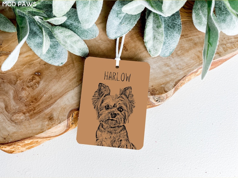 May include: A brown leather tag with a black and white illustration of a Yorkshire Terrier dog. The tag has the name "HARLOW" printed in black text.