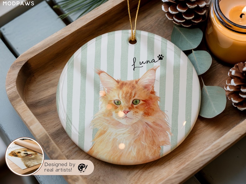 Pode incluir: Enfeite redondo de cer&acirc;mica com um retrato em aquarela de um gato laranja com olhos verdes, chamado Luna. O fundo tem listras verticais verdes e brancas. Uma corda dourada &eacute; anexada para pendurar. O enfeite &eacute; exibido em uma bandeja de madeira.