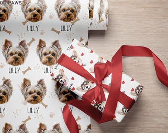 May include: White wrapping paper featuring a repeating pattern of Yorkshire Terrier faces, the name LILLY, and bone icons, alongside a gift box wrapped in the same paper with a red ribbon and the name Evie printed near small red heart icons.