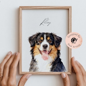 Op de afbeelding: Een ingelijst aquarelportret van een Berner Sennenhond met zwart, wit en bruin haar, met de naam Riley in zwarte schrijfletters erboven. De tekst MOD PAWS staat linksboven en een ronde badge bevat de tekst Designed By Real Artists.