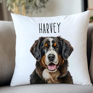Puede incluir: Coj&iacute;n cuadrado blanco con un retrato de acuarela de un perro de monta&ntilde;a bern&eacute;s. El perro tiene pelo negro, marr&oacute;n y blanco, con el nombre "HARVEY" impreso en negro encima. El coj&iacute;n est&aacute; sobre un sof&aacute; gris.