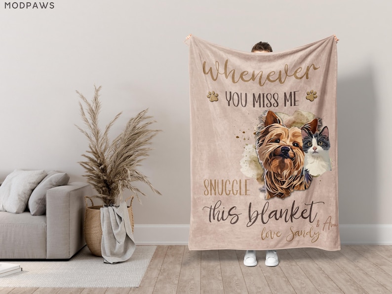 May include: A beige blanket with the text "Whenever you miss me, snuggle this blanket." The blanket features illustrations of a dog and a cat. The blanket is held up by a person wearing white shoes.