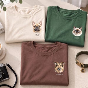 以下が含まれることがあります： クリーム色、ダークグリーン、ブラウンのクルーネックTシャツ3枚。各シャツの左胸にはペットの小さな詳細なイラストが描かれており、その下に名前がプリントされています。クリーム色のシャツにはDuke、グリーンのシャツにはCosmo、ブラウンのシャツにはBoomerと記されています。