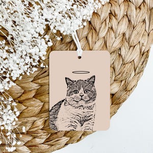 May include: A black and white illustration of a cat with a halo above its head. The cat is sitting on a light pink background.