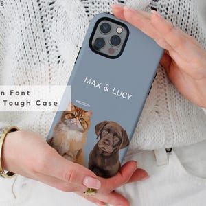 May include: Azure phone case with a custom pet portrait of a cat and a dog, with the names "MAX & LUCY" in a modern font. The case is held by a person wearing a white sweater.