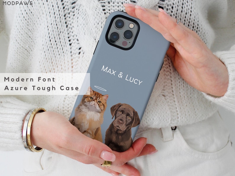 May include: Azure phone case with a custom pet portrait of a cat and a dog, with the names "MAX & LUCY" in a modern font. The case is held by a person wearing a white sweater.