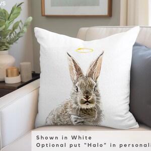 May include: White throw pillow with a watercolor illustration of a gray rabbit with a gold halo. The text "Shown in White" and "Optional put "Halo" in personalization" is below the image.