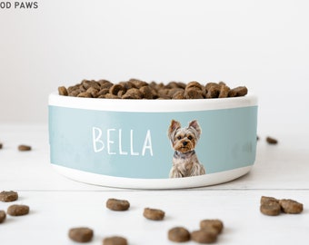 May include: A light blue ceramic dog bowl with the name "Bella" printed on it. A small Yorkshire Terrier dog is pictured on the bowl. The bowl is filled with brown dog food.