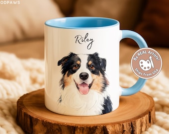 May include: A white ceramic mug with a light blue interior and handle, featuring a watercolor-style illustration of a black, white, and tan Australian Shepherd dog. The name Riley is printed in black script above the dog, and a circular badge reads By REAL Artists! Ships from USA.