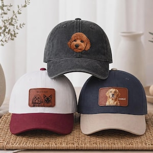 以下が含まれることがあります： 3つのベースボールキャップ：茶色の犬の刺繍が施されたチャコールグレーのキャップ、マルーン色のつばと2匹の犬が描かれた長方形のレザーパッチが付いた白いキャップ、ベージュのつばと犬が描かれたレザーパッチが付いたネイビーブルーのキャップ。