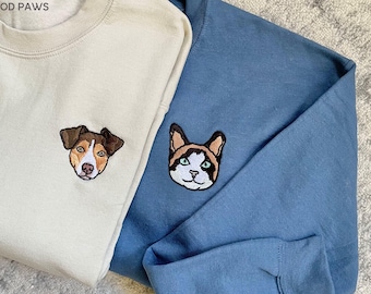 May include: A cream-colored sweatshirt featuring an embroidered brown and white dog face and a blue sweatshirt featuring an embroidered calico cat face. The text MOD PAWS is printed in the top left corner of the cream sweatshirt.
