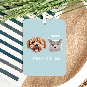 May include: A light blue car air freshener with a photo of a brown dog and a gray cat. The text "DOLLY & LUNA" is printed below the photos.