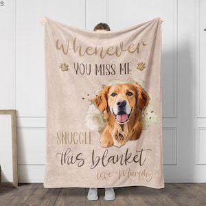 May include: A beige blanket featuring a golden retriever illustration with the text "Whenever you miss me, snuggle this blanket, love Murphy." The blanket has paw print accents and is held up by a person.