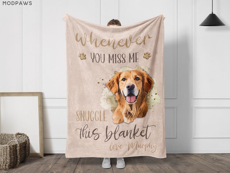 May include: A beige blanket featuring a golden retriever illustration with the text "Whenever you miss me, snuggle this blanket, love Murphy." The blanket has paw print accents and is held up by a person.