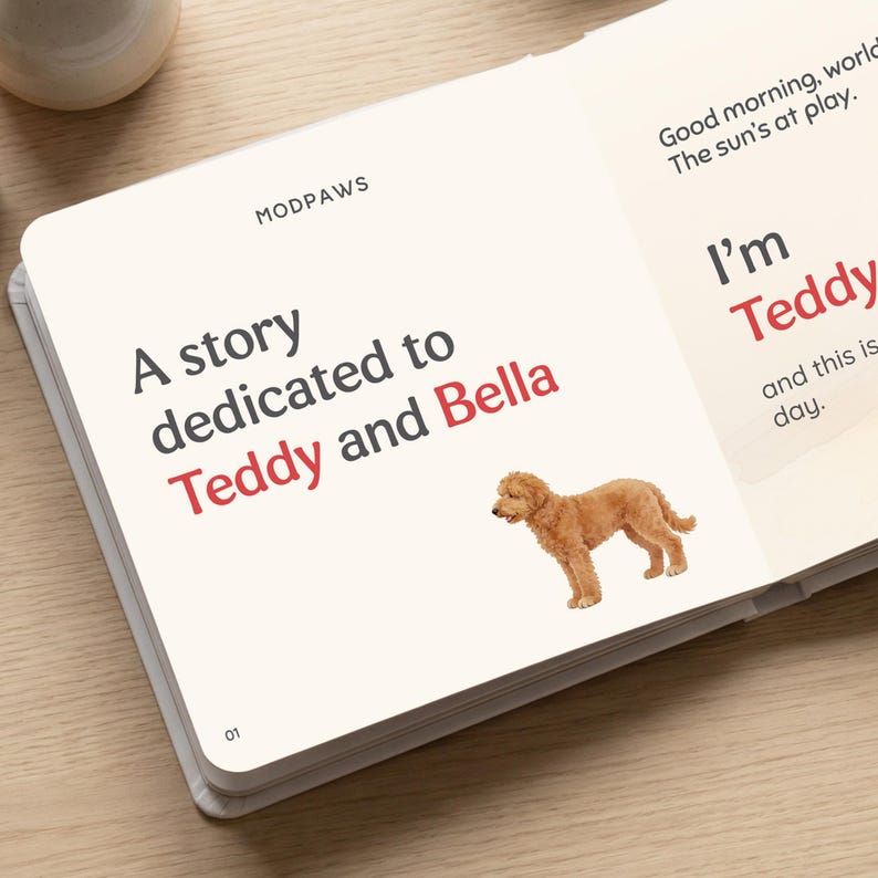 May include: An open book with the title "A story dedicated to Teddy and Bella" and the Modpaws logo. The text is in black and red. A golden doodle illustration is on the page. The text "Good morning, world. The sun's at play" is also visible.