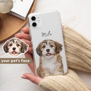 Könnte beinhalten: Eine transparente Smartphone-Hülle mit einer individuellen Illustration eines braun-weißen Welpen, wobei der Name Mila in schwarzer Schreibschrift über dem Hund steht. Der Welpe hat Schlappohren, dunkle Augen und eine rosa Zunge.