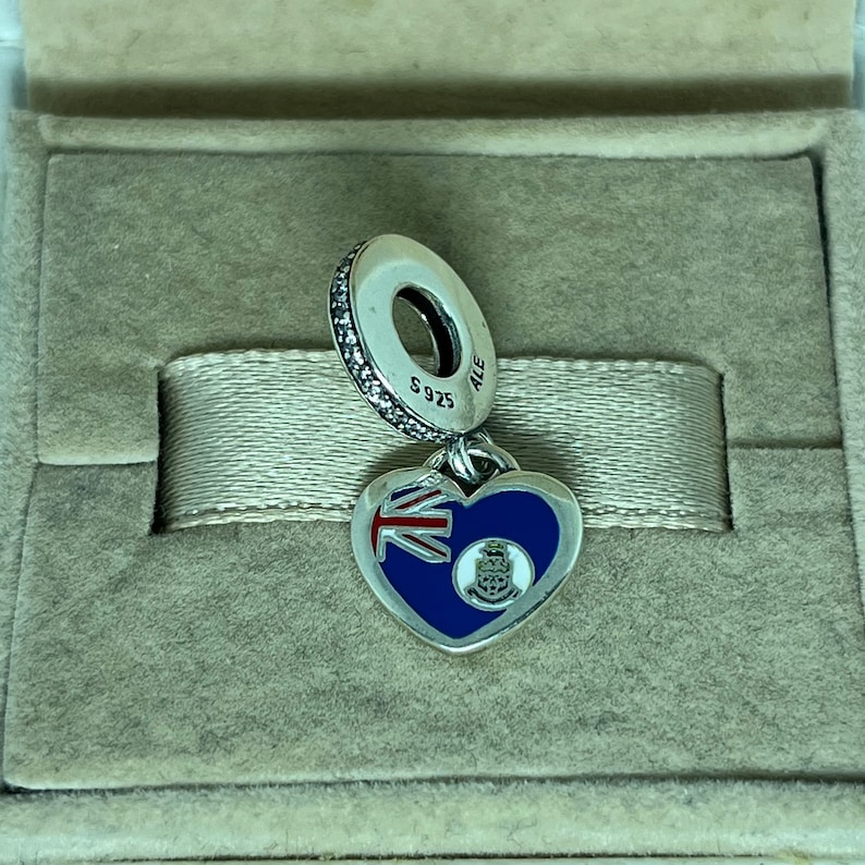 May include: Silver charm in the shape of a heart with the flag of the British Virgin Islands on one side and the territory's coat of arms on the other. The charm is attached to a silver bead with the inscription "S925 ALE".