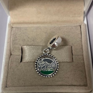 May include: A silver charm with a green and black enamel design of Mount Rushmore. The charm is in a white box with a white ribbon.