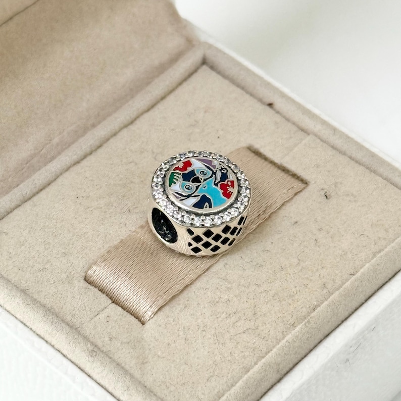 May include: A silver charm with a colorful enamel design of a bird and flowers. The charm is surrounded by a row of clear cubic zirconia stones.