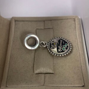 May include: Silver charm featuring a black and white enamel design of a Hollywood sign with fireworks. The charm has a silver ring for attaching to a bracelet.