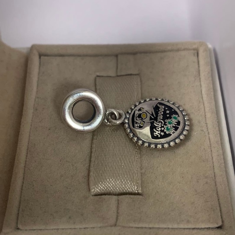 May include: Silver charm featuring a black and white enamel design of a Hollywood sign with fireworks. The charm has a silver ring for attaching to a bracelet.