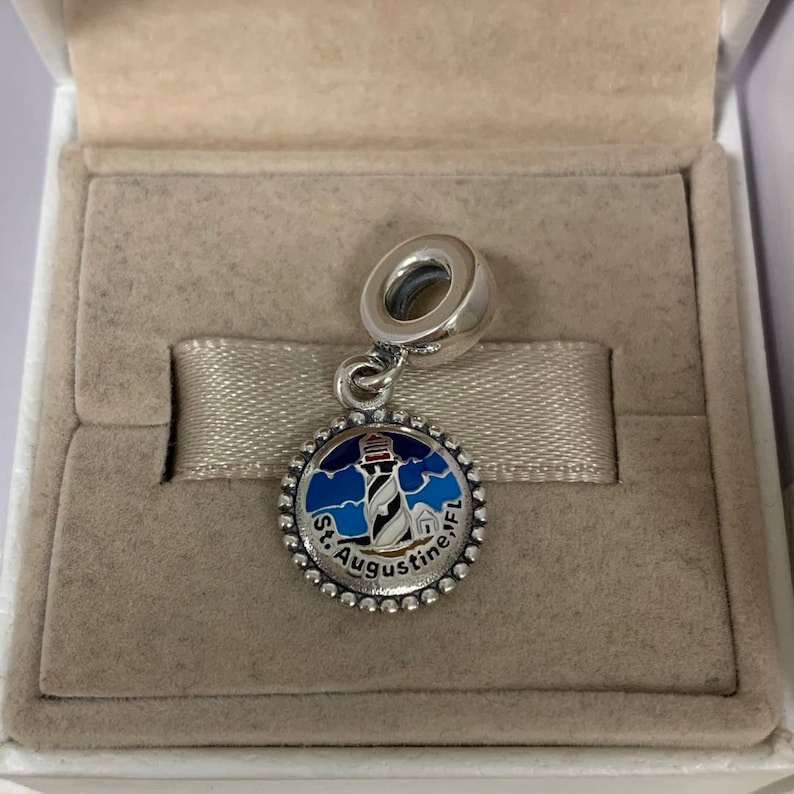 K&ouml;nnte beinhalten: Silberner Anh&auml;nger mit einem blauen, wei&szlig;en und roten Emaille-Leuchtturm-Design. Der Anh&auml;nger tr&auml;gt den Text "St. Augustine, FL" am Rand.