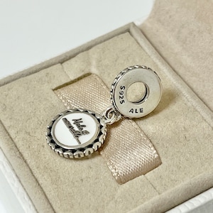 Puede incluir: Encanto de plata con un c&iacute;rculo de esmalte blanco que dice "Make a memory..." y un c&iacute;rculo de plata en la parte posterior que dice "S925 ALE".