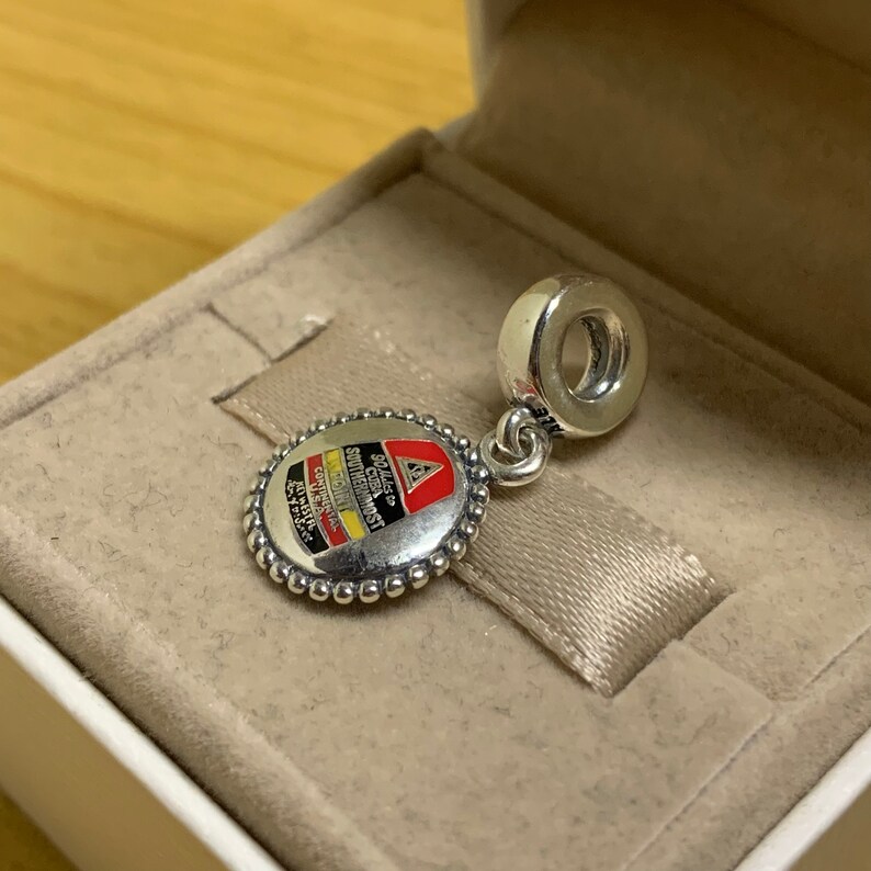 May include: Silver charm with a round, white enamel design featuring a red and yellow logo with the text "92nd  CHICAGO  SOUTHWESTERN  CONTINENTAL  AIRLINES  1971-1979".