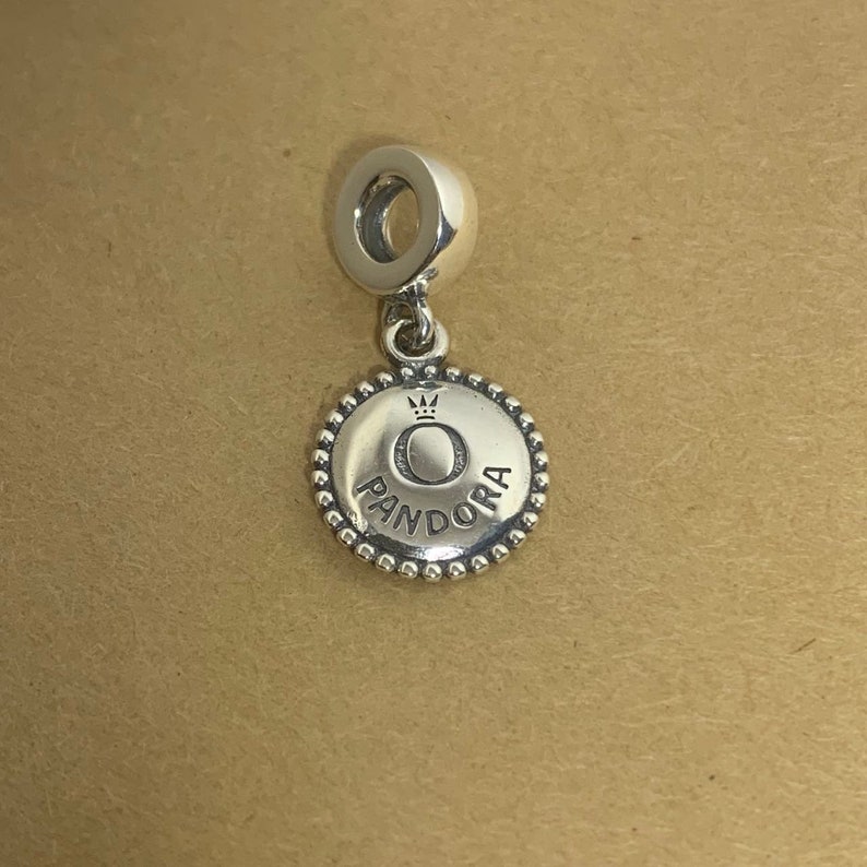 May include: Silver charm with a round, beaded edge. The charm features a silver circle with a crown and the word "PANDORA" inscribed around it.