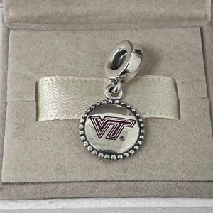 May include: Silver charm with a red and white VT logo on a round silver charm with a beaded border. The charm is in a white box.