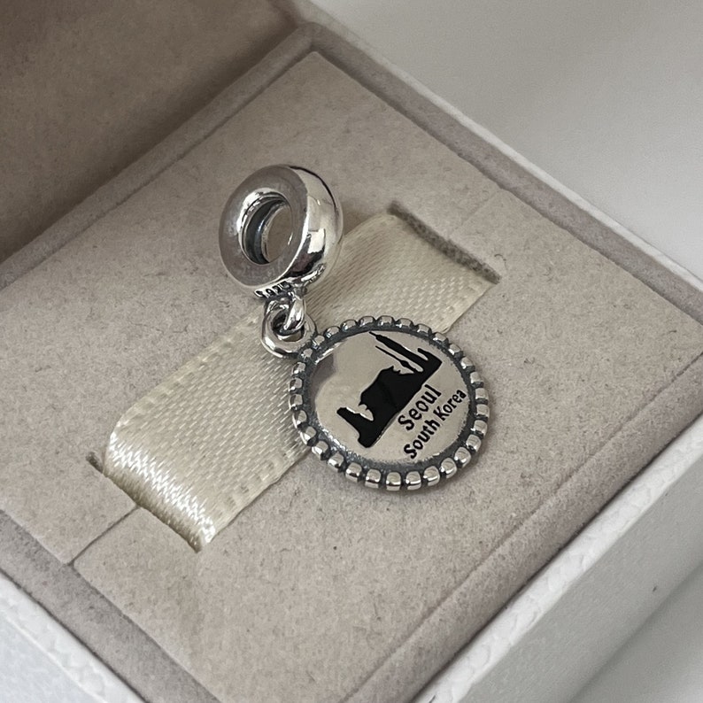 May include: Silver charm featuring a black and white image of the Seoul skyline with the text "Seoul South Korea".
