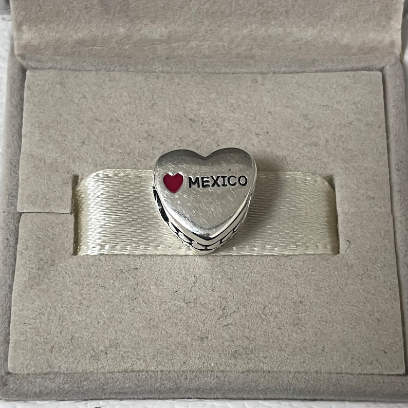 Puede incluir: Encanto de plata en forma de coraz&oacute;n con un coraz&oacute;n rojo y la palabra "MEXICO" en &eacute;l.
