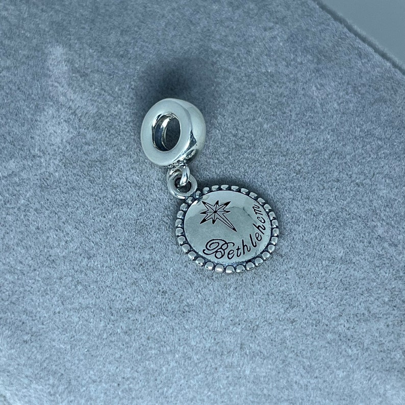 May include: Silver charm with a star and the word "Bethlehem" engraved on a round disc.