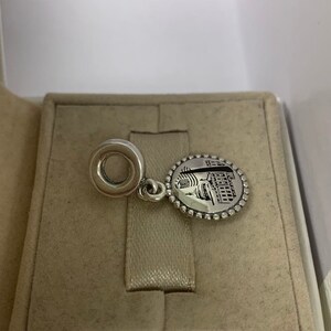 Puede incluir: Encanto de plata con una imagen detallada de un edificio y un c&iacute;rculo en la parte superior para sujetarlo a una pulsera.