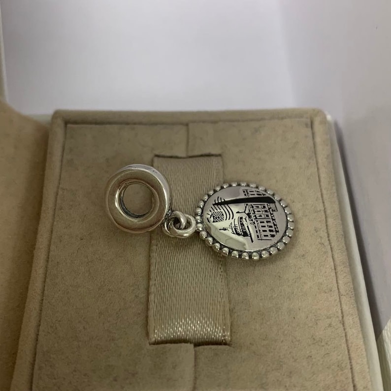 Puede incluir: Encanto de plata con una imagen detallada de un edificio y un c&iacute;rculo en la parte superior para sujetarlo a una pulsera.