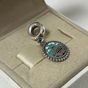May include: Silver charm featuring a blue and white enamel design of a building with the text "Folly Beach" on it.