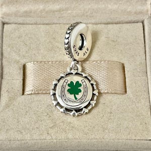 May include: Silver charm with a green four-leaf clover and horseshoe design. The charm has a silver bead with the text "S925 ALE" on it.