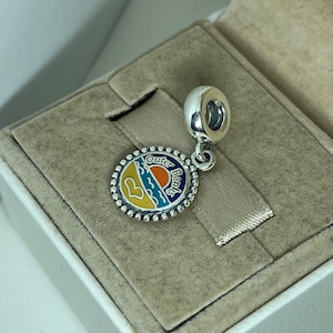 K&ouml;nnte beinhalten: Silberner Anh&auml;nger mit einem blauen, gelben und orangefarbenen Emaille-Design, das einen Sonnenuntergang &uuml;ber dem Meer darstellt. Der Anh&auml;nger tr&auml;gt die Worte "Outer Banks" um den Rand herum.
