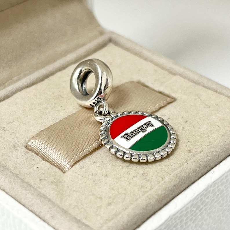 May include: Silver charm with a red, white, and green enamel circle featuring the Hungarian flag and the word "Hungary".