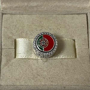 Puede incluir: Un charm de plata con un dise&ntilde;o de esmalte rojo y verde de la bandera portuguesa. El charm est&aacute; rodeado por un c&iacute;rculo de piedras de circonita c&uacute;bica transparentes.