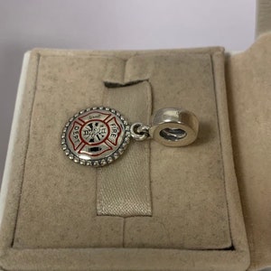 May include: Silver charm with a red and black enamel firefighter emblem. The emblem features a fire hydrant, an axe, and the words "FIRE DEPT."