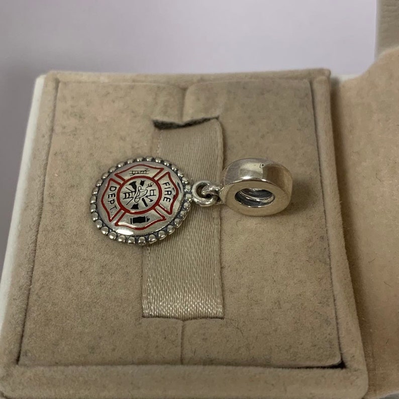 May include: Silver charm with a red and black enamel firefighter emblem. The emblem features a fire hydrant, an axe, and the words "FIRE DEPT."